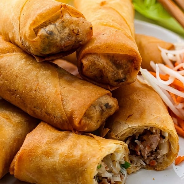 Golden-brown spring rolls, one cut open to show the savory filling, with pickled vegetables and chopsticks.